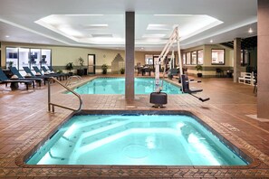 En indendørs swimmingpool med liggestole, et spabad og en trappe til et plan over.