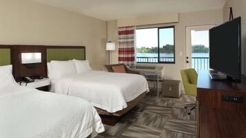 A hotel room with two beds, a desk, a chair, a TV, and a view of a lake.