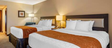 Habitación de hotel con dos camas, cada una con ropa de cama blanca y mantas marrones. Hay lámparas de noche y un cuadro en la pared.