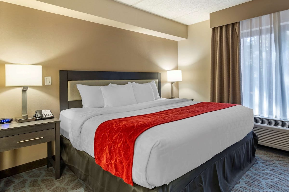Ein Hotelzimmer mit einem großen Bett, zwei Nachttischlampen, einem Nachttisch mit Telefon und einem Fenster mit Vorhängen.