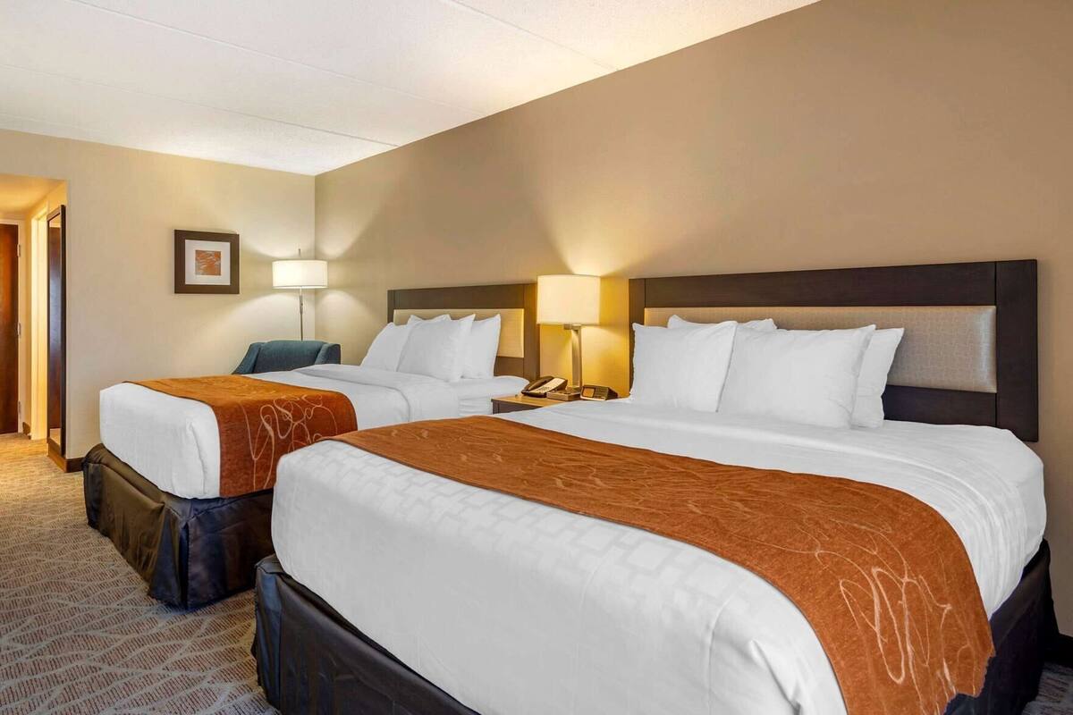 Ein Hotelzimmer mit zwei Betten, jeweils mit Kopfteil, Nachttischen mit Lampen und einem Teppichboden.