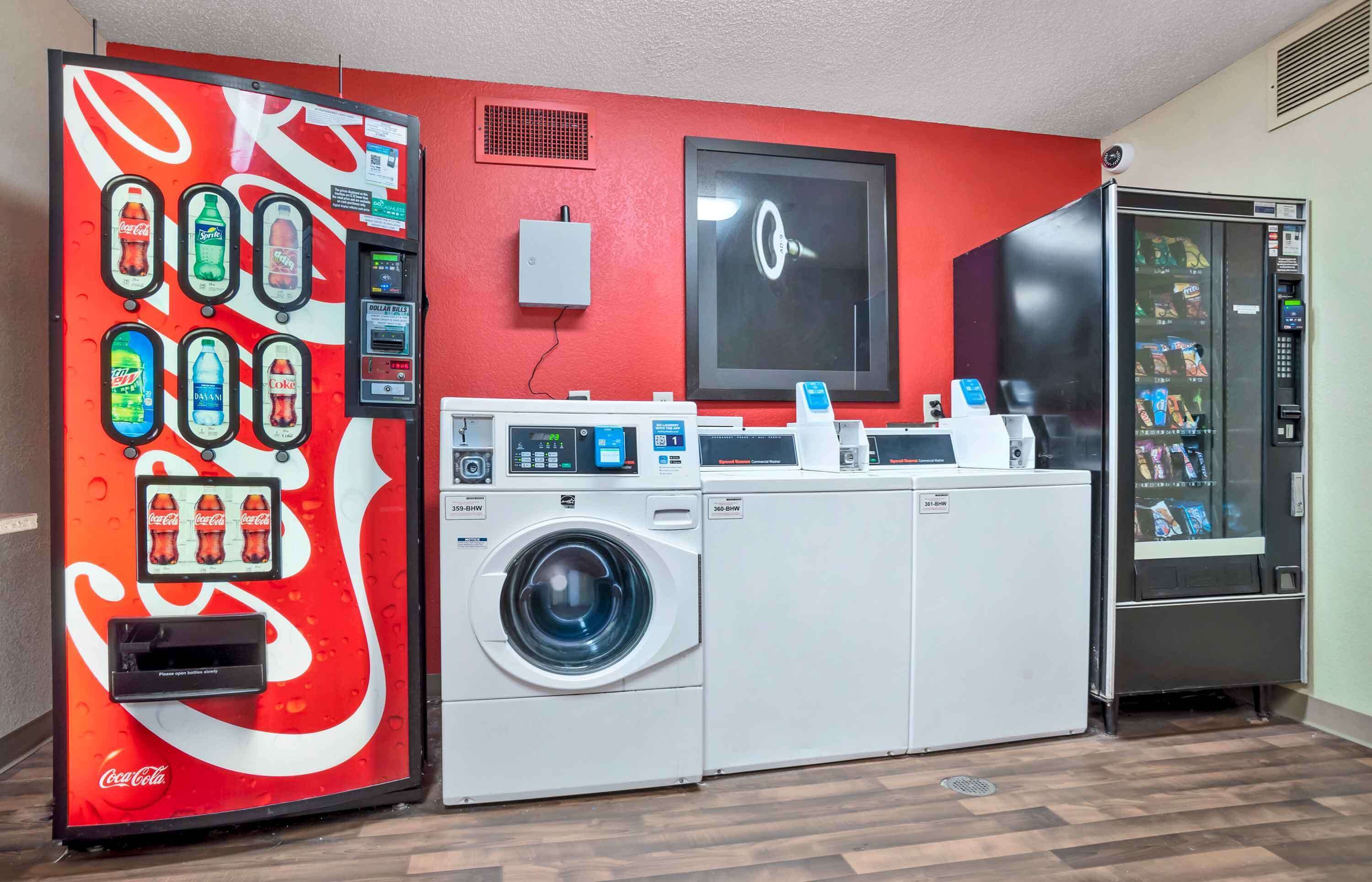 Un área de lavandería con máquina expendedora de Coca-Cola, lavadora y refrigerador.