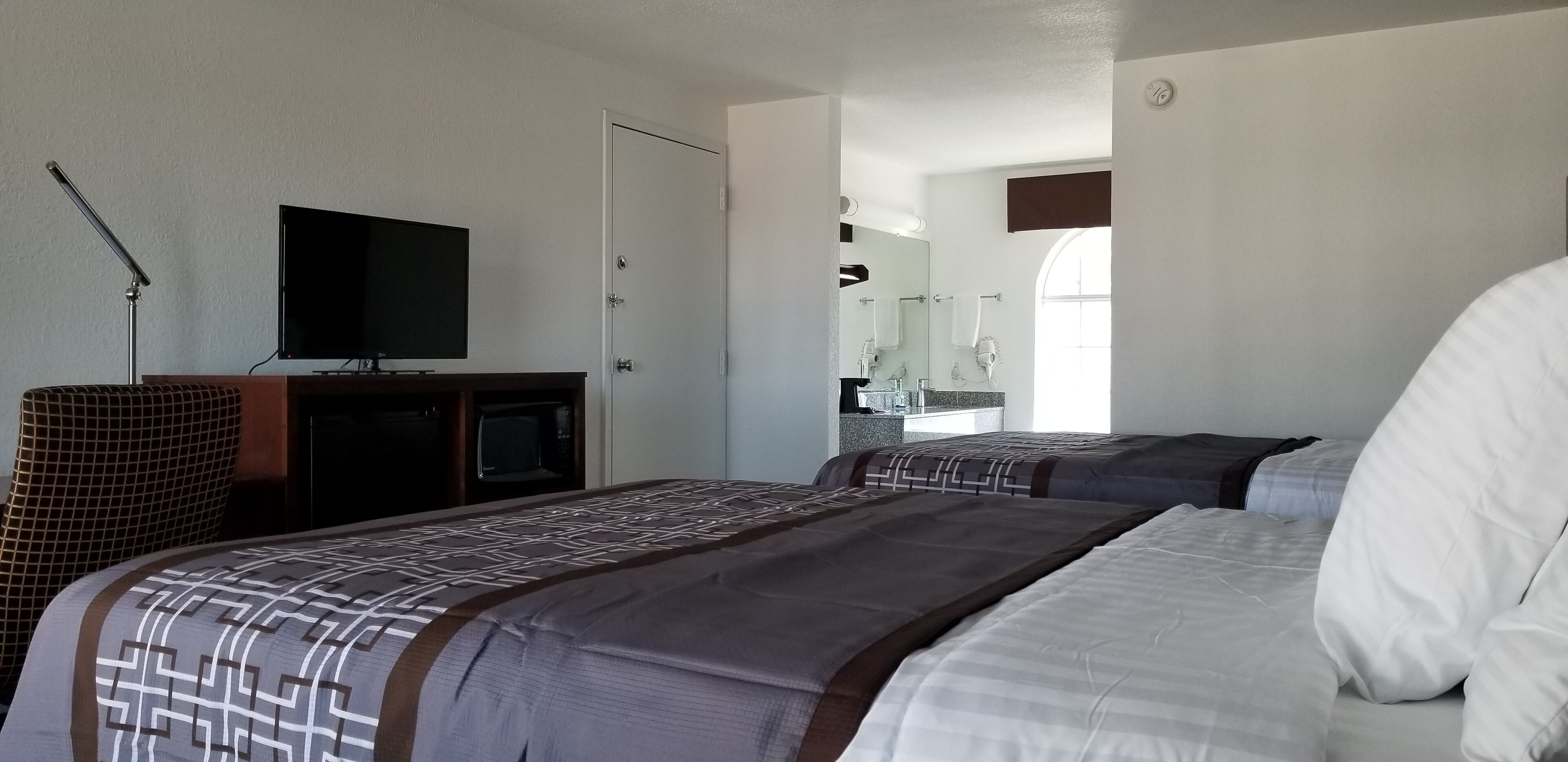 Une chambre d’hôtel avec deux lits, une télévision, un bureau et une salle de bain visible à travers une porte ouverte.