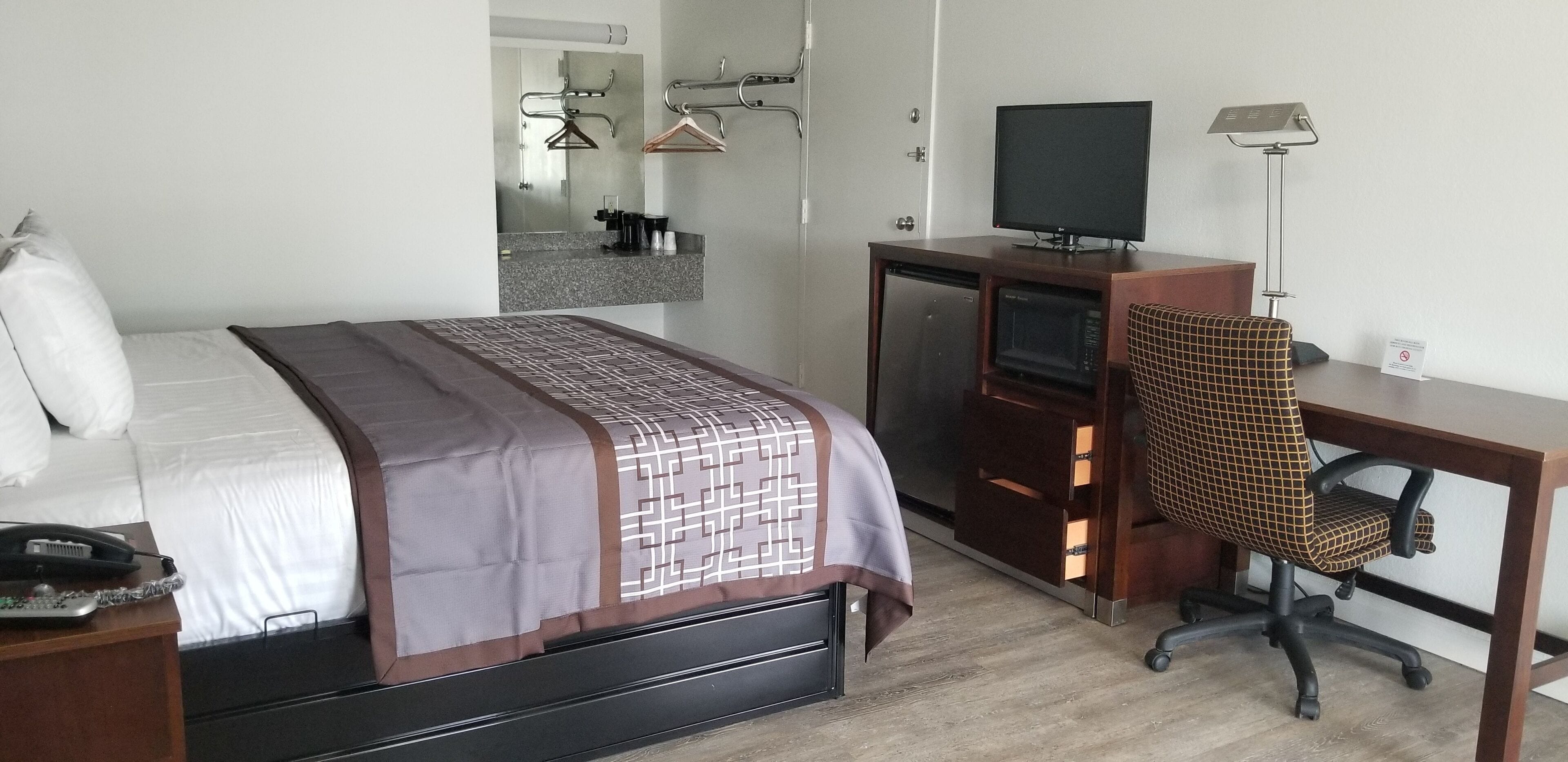A hotel room with a bed, a desk with a chair, a television, a microwave, and a small refrigerator.