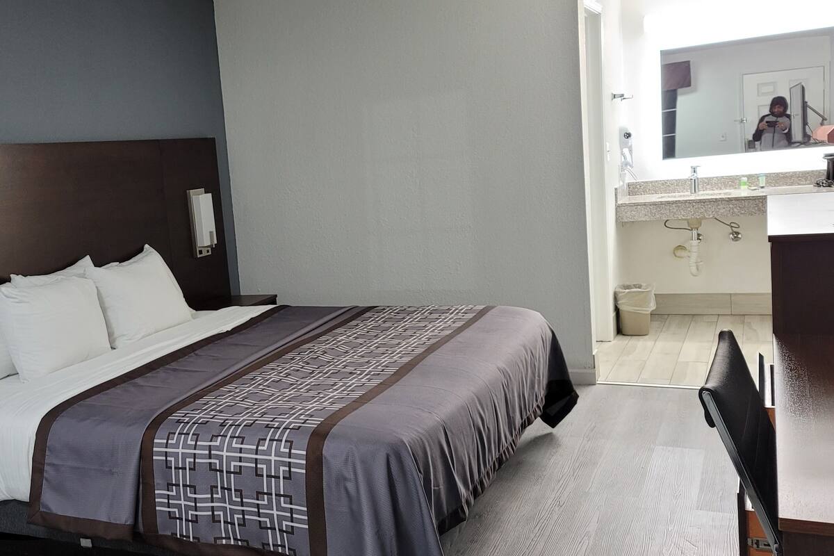 A hotel room with a large bed, a bedside table with a phone, a mirror, and a bathroom visible in the background.