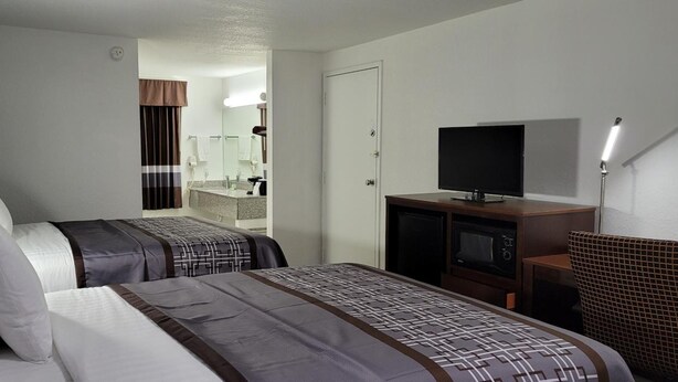 A hotel room with two beds, a TV, a desk, and a bathroom visible in the background. - Key West Inn - Boaz (Boaz)