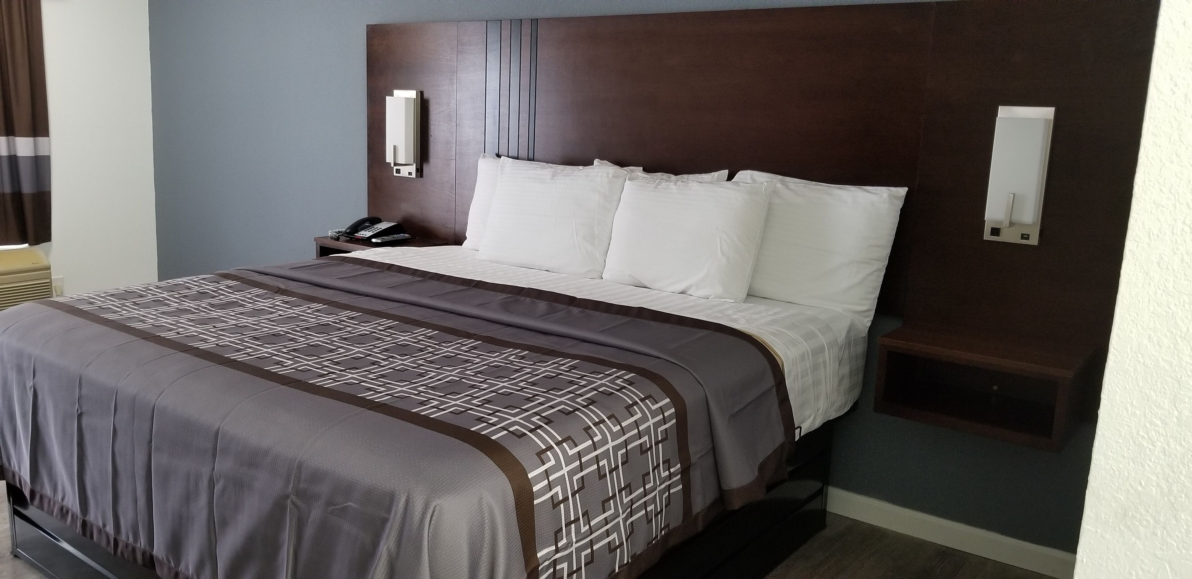 Camera d'albergo con un letto grande, un comodino, un telefono e una lampada a parete.
