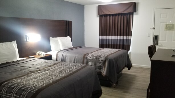 Hotellihuone, jossa on kaksi sänkyä, työpöytä, tuoli, puhelin ja ikkuna, jossa on verhot.