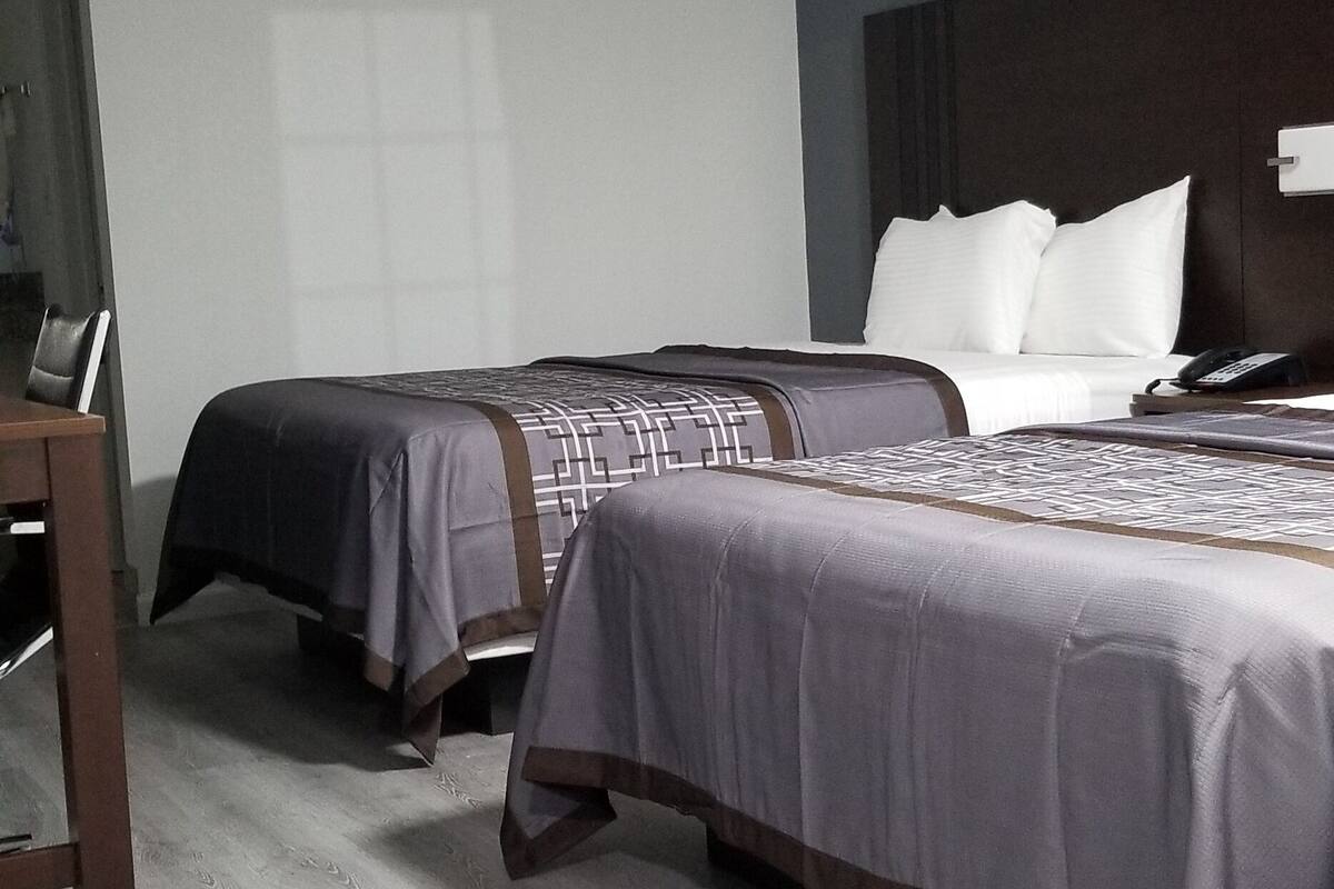 A hotel room with two beds, a wooden desk, and a large window.