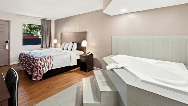 Ein modernes Hotelzimmer mit einem großen Bett, einer separaten Sitzecke, einer Badewanne und Blick ins Freie.