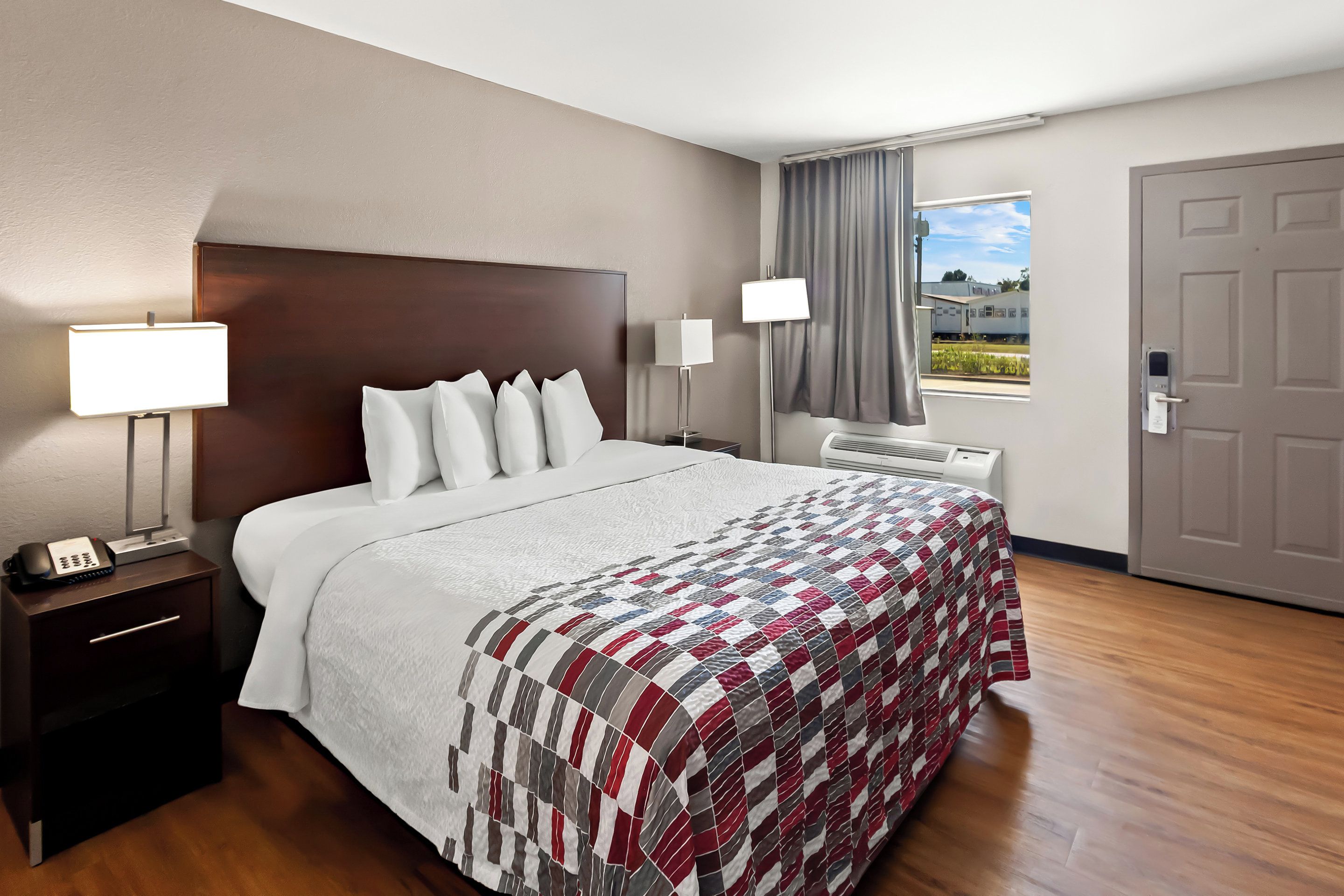 Une chambre d’hôtel avec un grand lit, deux tables de chevet avec des lampes, une fenêtre avec des rideaux et une porte.