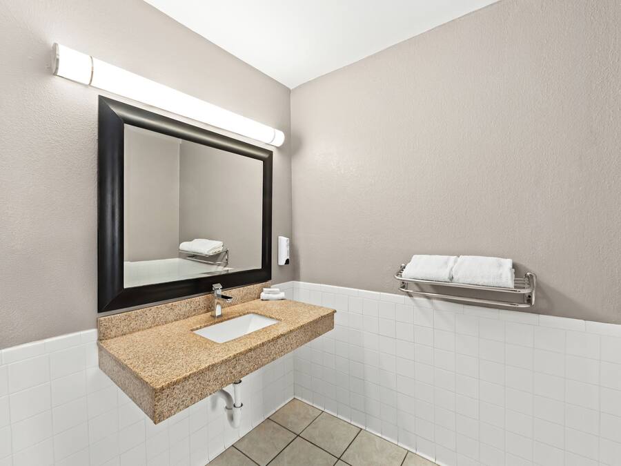 A bathroom with a granite countertop sink, a large mirror, and a towel rack.