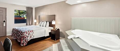 A modern hotel room with a large bed, a separate sitting area, a bathtub, and a view of the outdoors.
