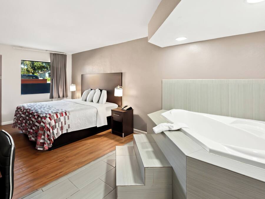 A modern hotel room with a large bed, a separate sitting area, a bathtub, and a view of the outdoors.