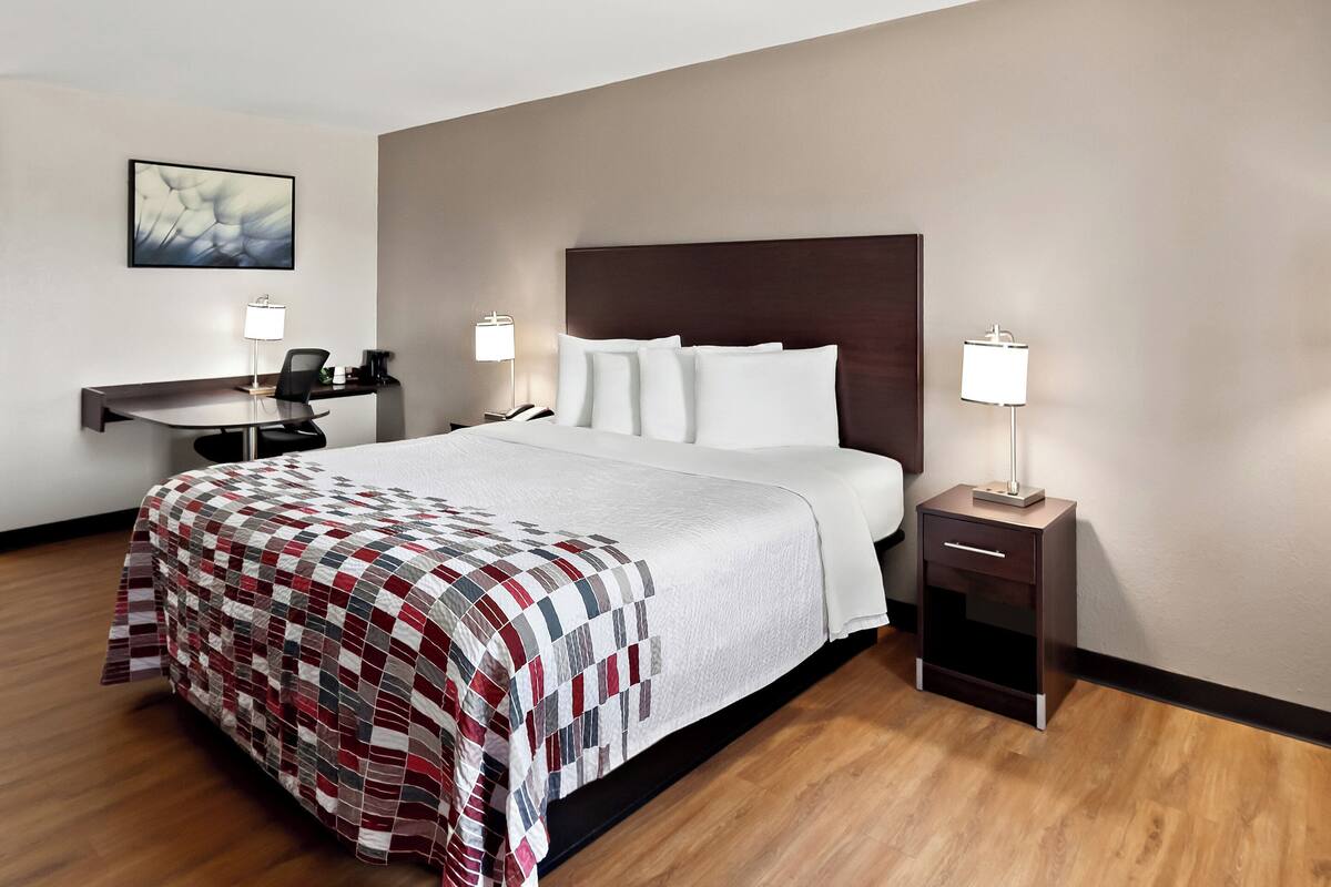 A hotel room with a large bed, two bedside tables with lamps, a desk with a chair, and a framed picture on the wall.