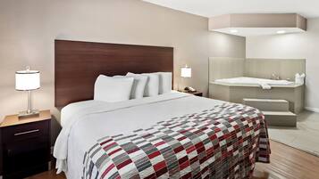 Une chambre d’hôtel avec un grand lit, une table de chevet avec une lampe, une salle de bain avec une baignoire et un miroir.