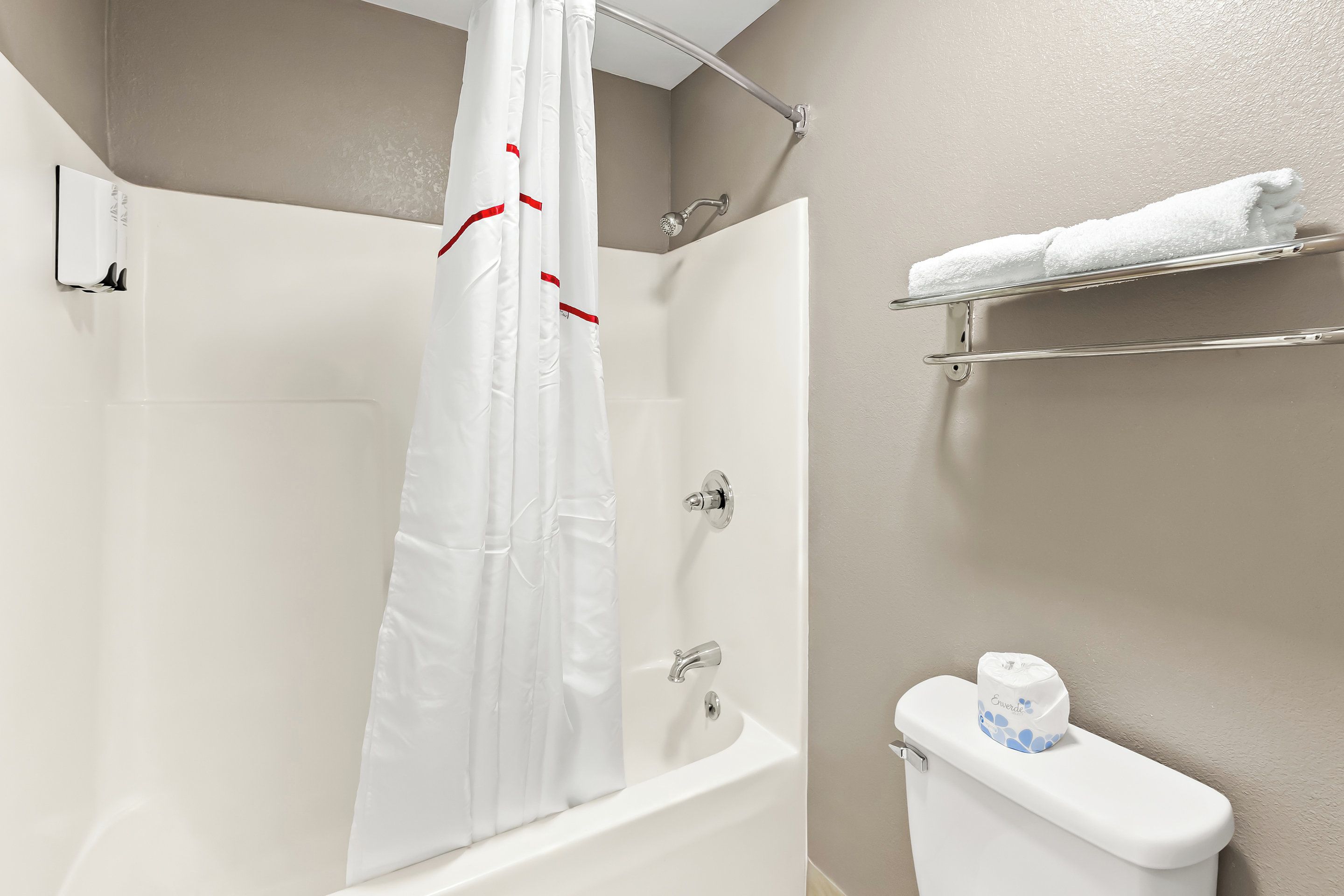 A bathroom with a bathtub, a shower curtain, a toilet, and a towel rack.