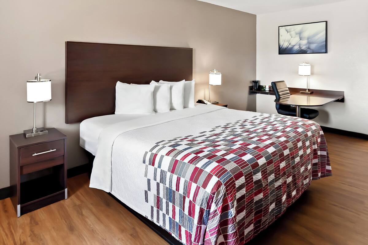 A hotel room with a large bed, bedside tables with lamps, a desk with a chair, and a wall-mounted shelf.