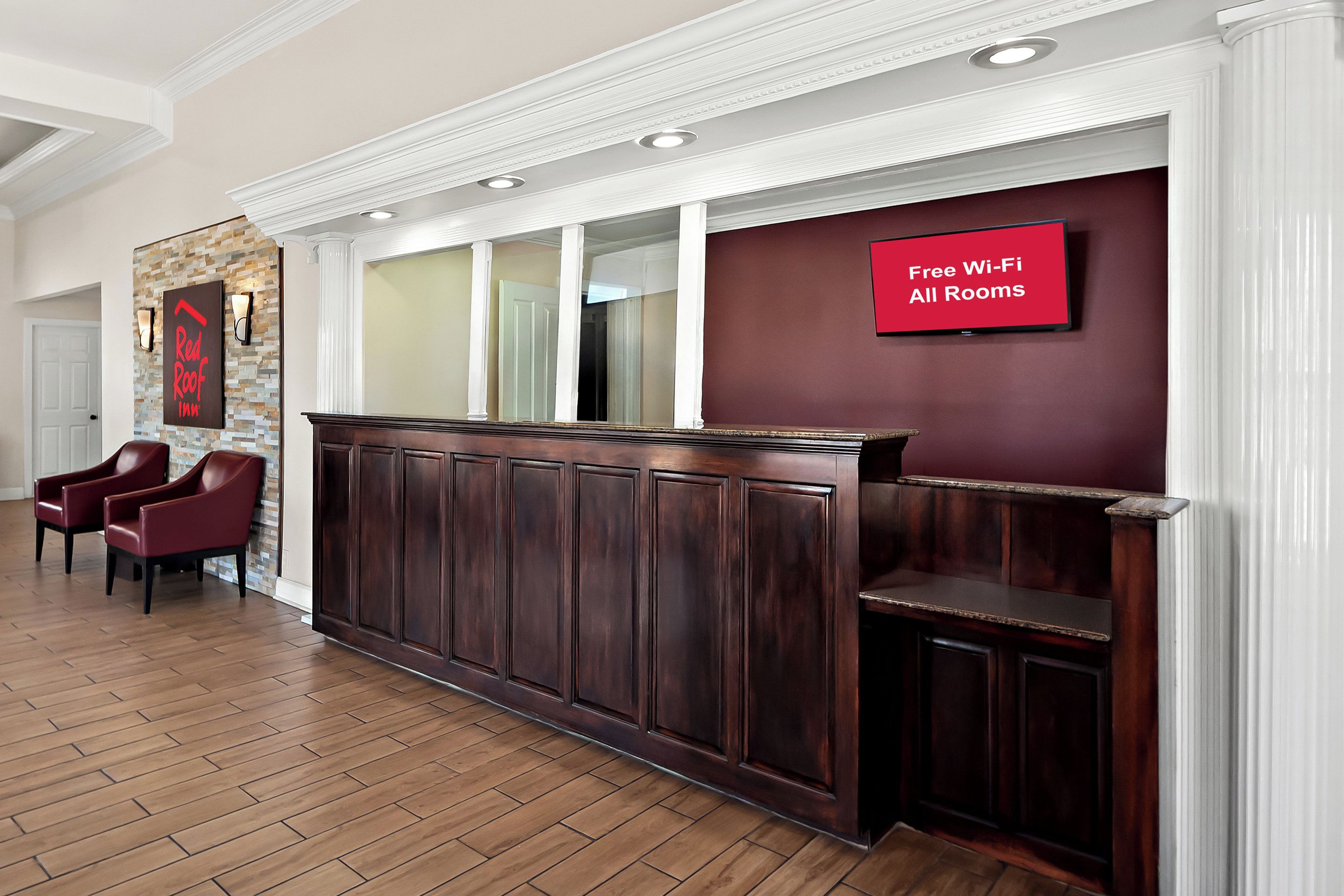 A reception area with a dark wood reception desk, a red sign indicating free Wi-Fi, and two red leather chairs.