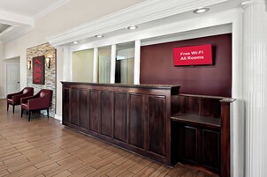 Uma área de recepção com um balcão de madeira escura, uma placa vermelha que indica Wi-Fi gratuito e duas poltronas de couro vermelho.