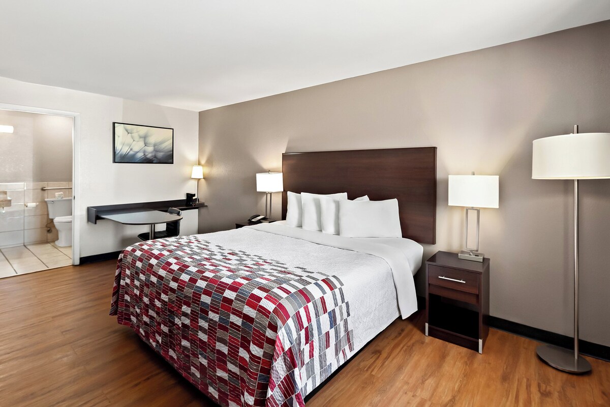 A hotel room with a bed, bedside tables, a desk, and a lamp.