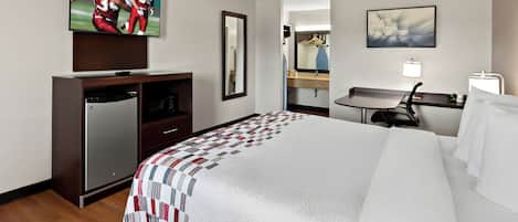 Una habitación de hotel con una cama grande, un televisor en la pared, un escritorio con una silla, un espejo y un cuadro.