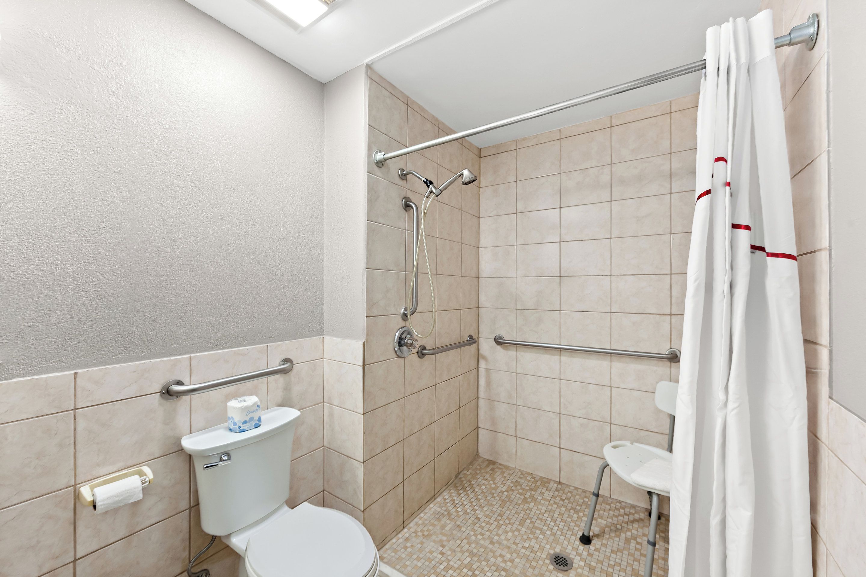 A small, modern bathroom with a toilet, a shower with a grab bar, and a white shower curtain.