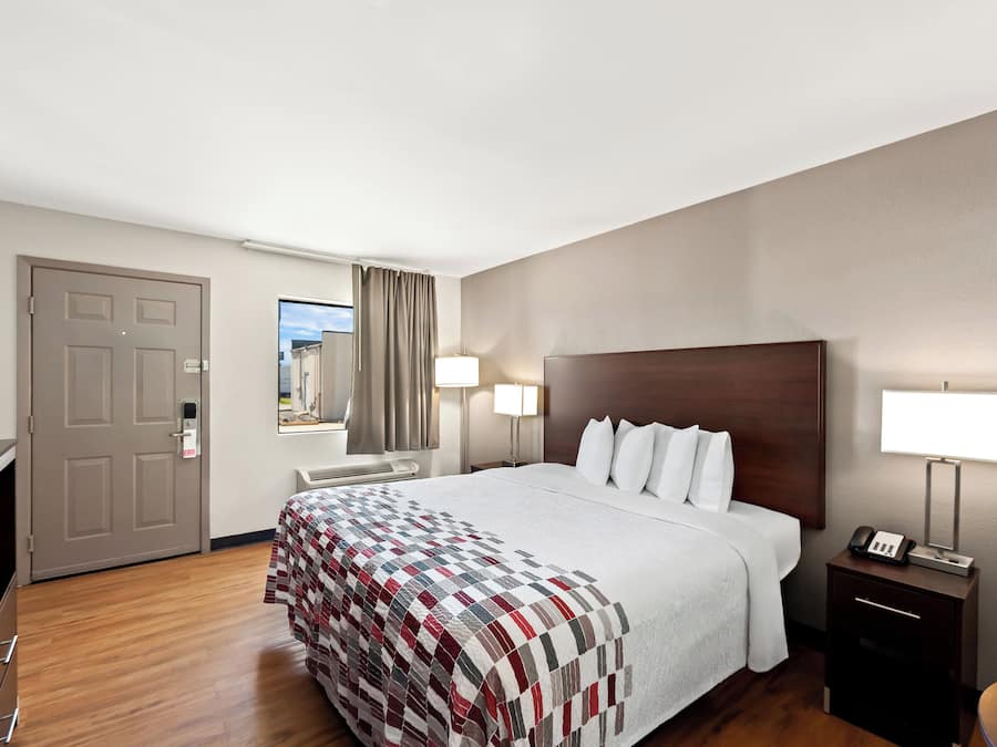 Ett hotellrum med en stor säng, ett skrivbord, en stol, en lampa och utsikt över omgivningarna.