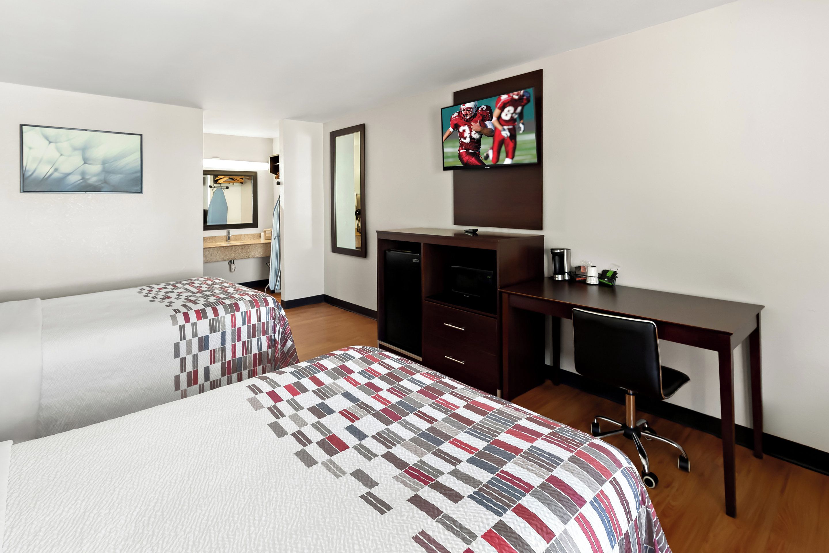 Una habitación de hotel con dos camas, un escritorio, una silla, un televisor y un espejo.