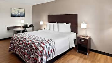 A hotel room with a large bed, two bedside tables with lamps, a desk with a chair, and a framed picture on the wall.