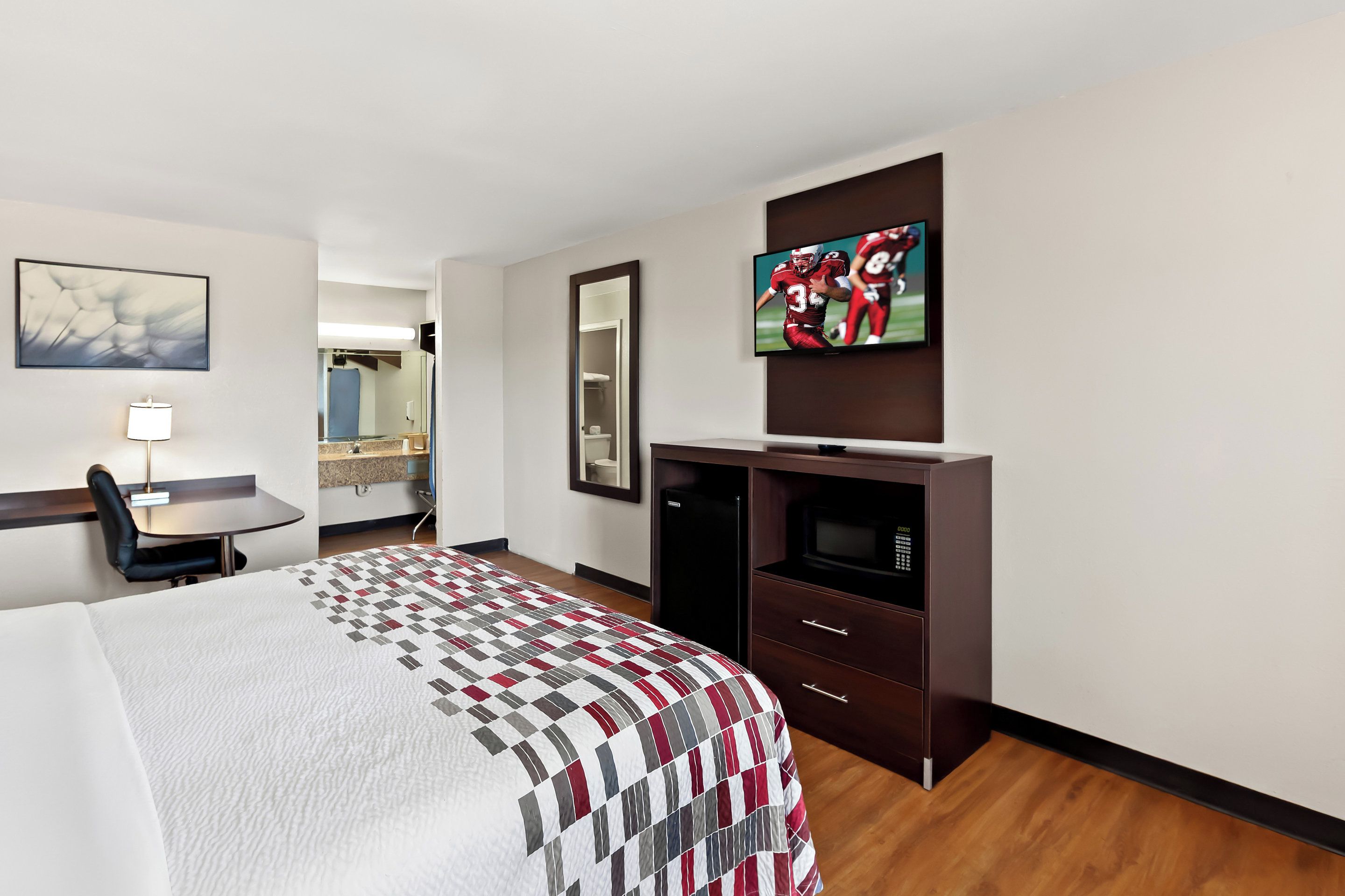 Habitación de hotel con cama, escritorio, silla, televisor, espejo y armario.