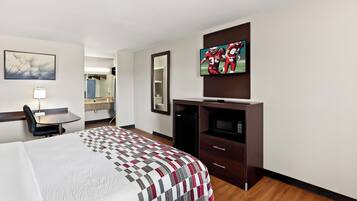 Habitación de hotel con cama, escritorio, silla, televisor, espejo y armario.