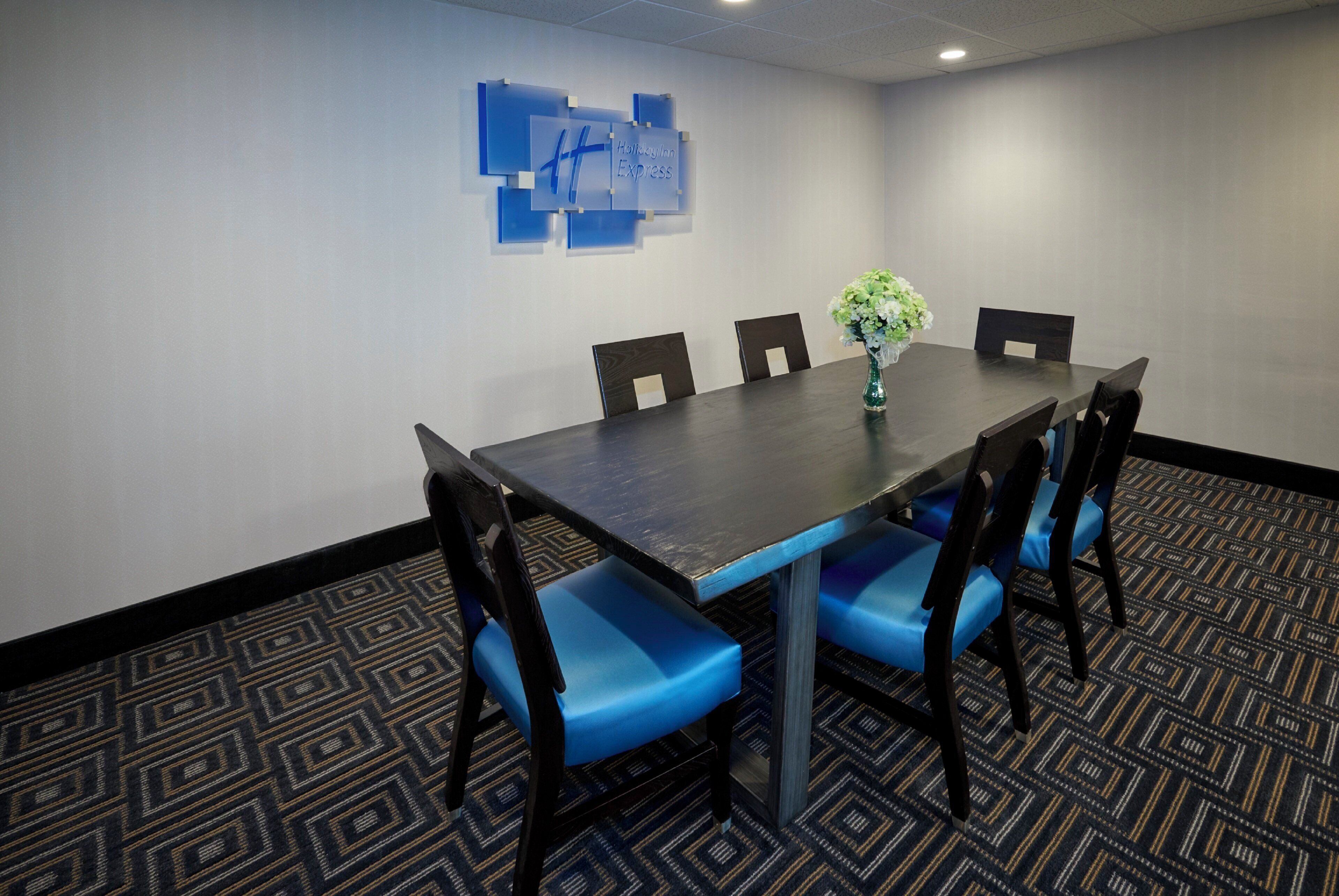 A conference room with a dark wooden table, blue upholstered chairs, and a floral arrangement.