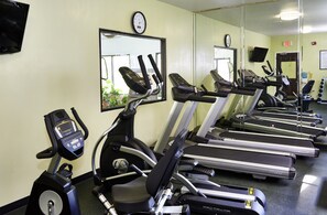 Un gimnasio con cintas de correr, bicicletas estáticas y un espejo grande.