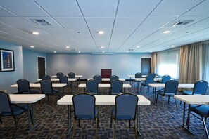 A conference room with multiple tables and chairs, a carpeted floor, and a blue wall with a framed picture. - Holiday Inn Express & Suites Birmingham South - Pelham by IHG (Pelham)