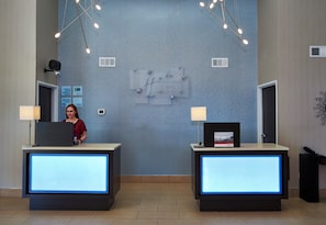 Un mostrador de recepción con una pantalla digital, un reloj y un cartel que indica los horarios de registro de entrada y salida.