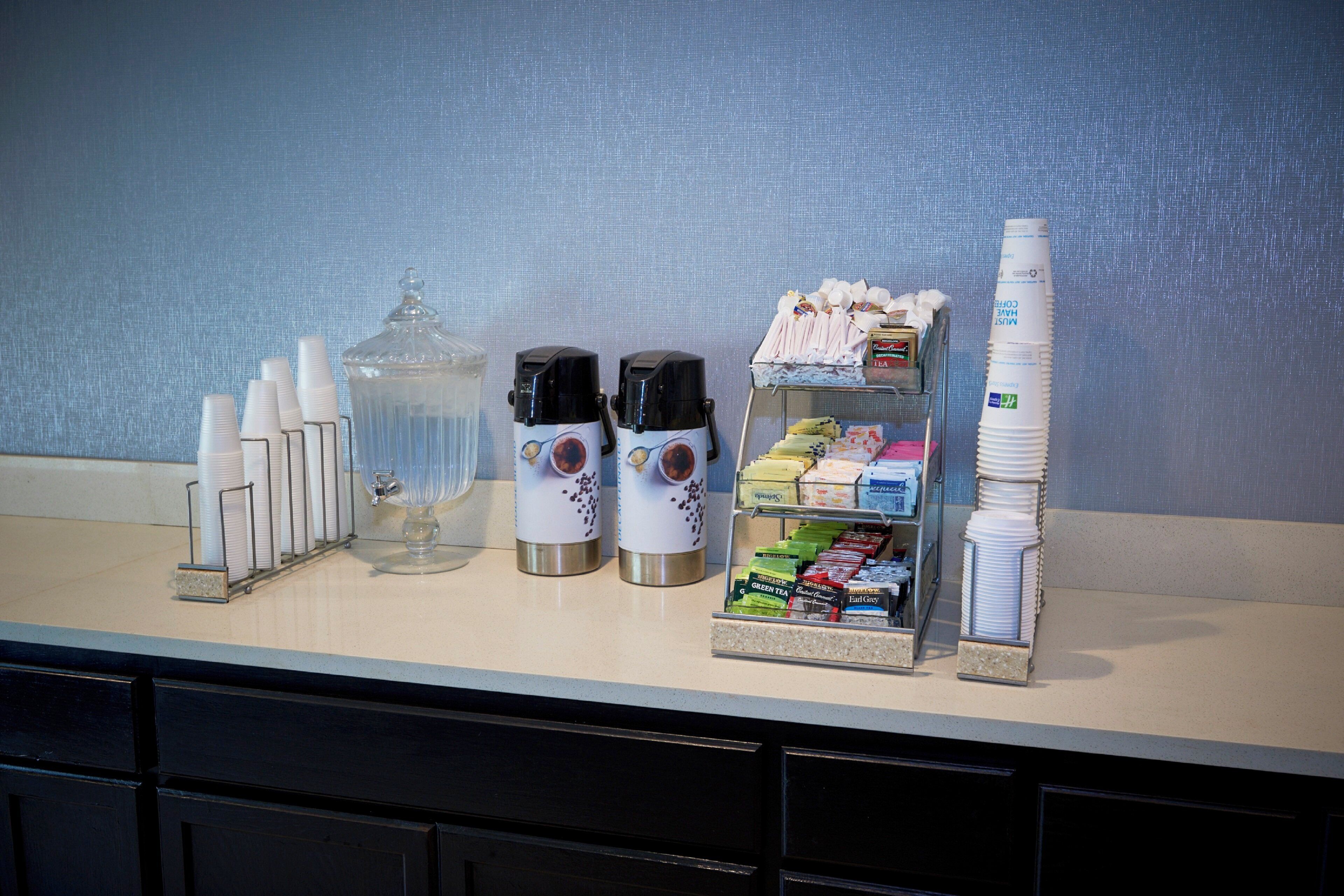 A coffee station with coffee makers, cups, and a variety of tea and coffee products.