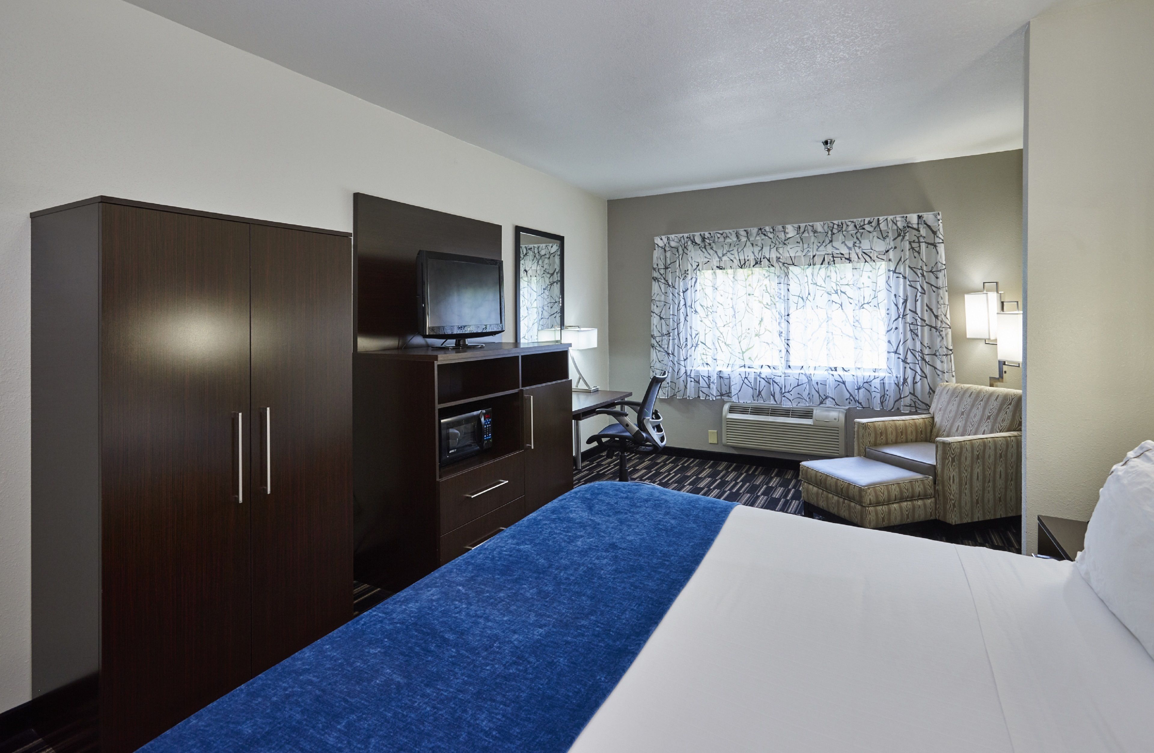 A hotel room with a bed, a desk with a computer, a TV, a wardrobe, and a chair.