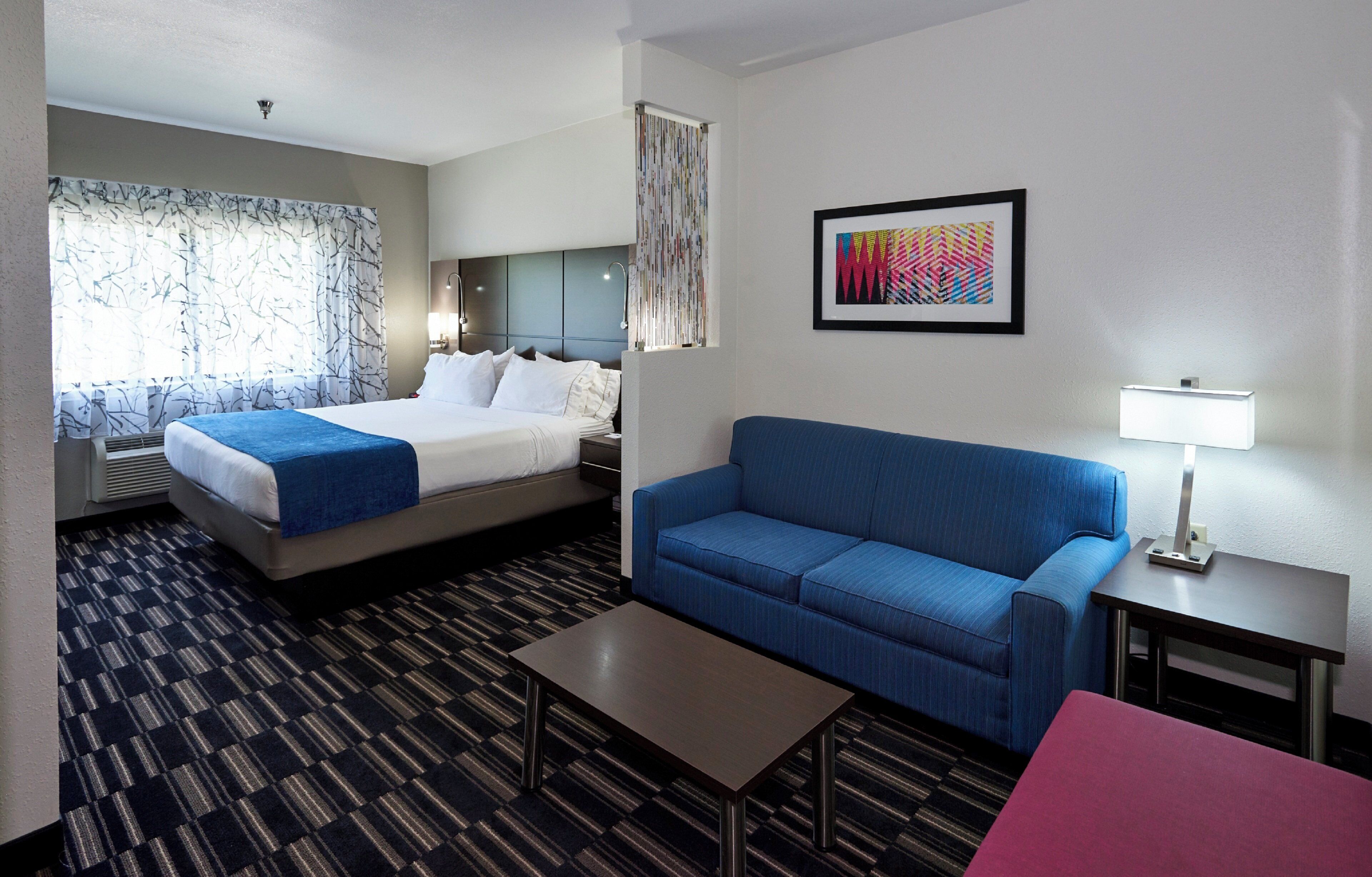 A hotel room with a bed, a blue sofa, a small table, a lamp, and a framed picture on the wall.
