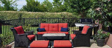 An outdoor patio with a black wicker sofa set, a small table, and a grill.