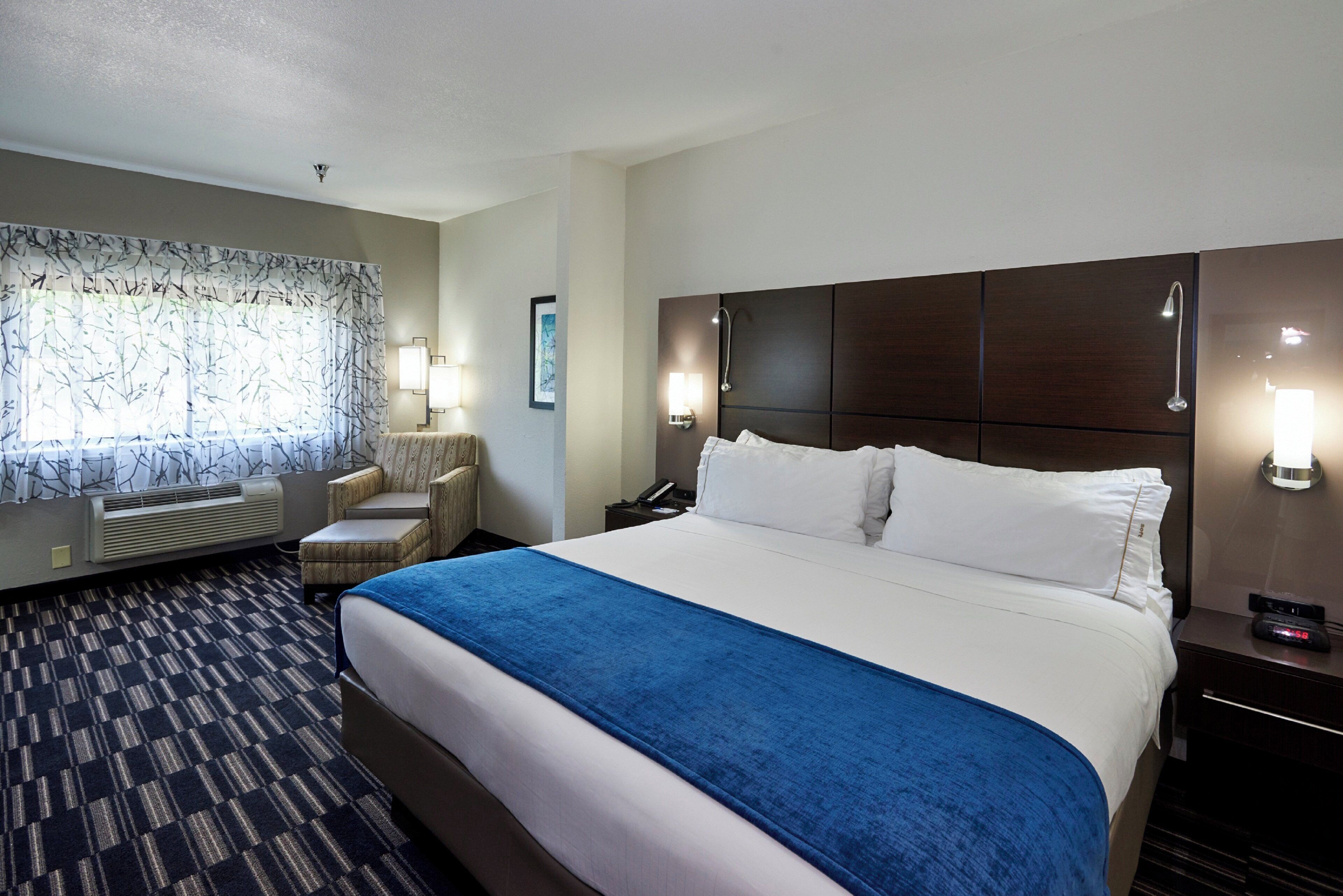 A hotel room with a large bed, a chair, a desk, and a window with a curtain.