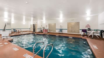 An indoor swimming pool with clear water, a diving board, and a lifeguard chair.