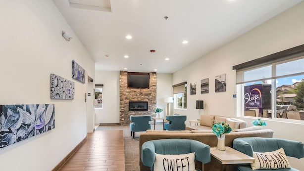 A hotel lobby with a stone fireplace, comfortable seating, artwork on the walls, and a sign for the Sleep Inn by Choice Hotels.