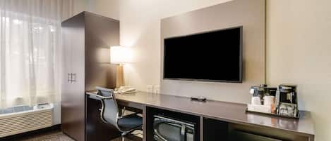 A hotel room with a desk, chair, flat-screen TV, microwave, mini-fridge, and coffee maker.