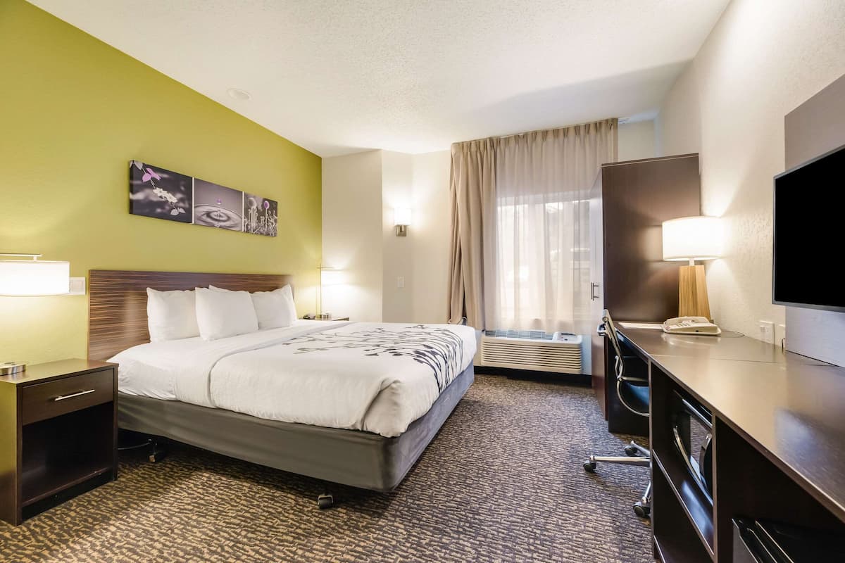 A hotel room with a bed, bedside tables, a desk, a TV, and a window with curtains.