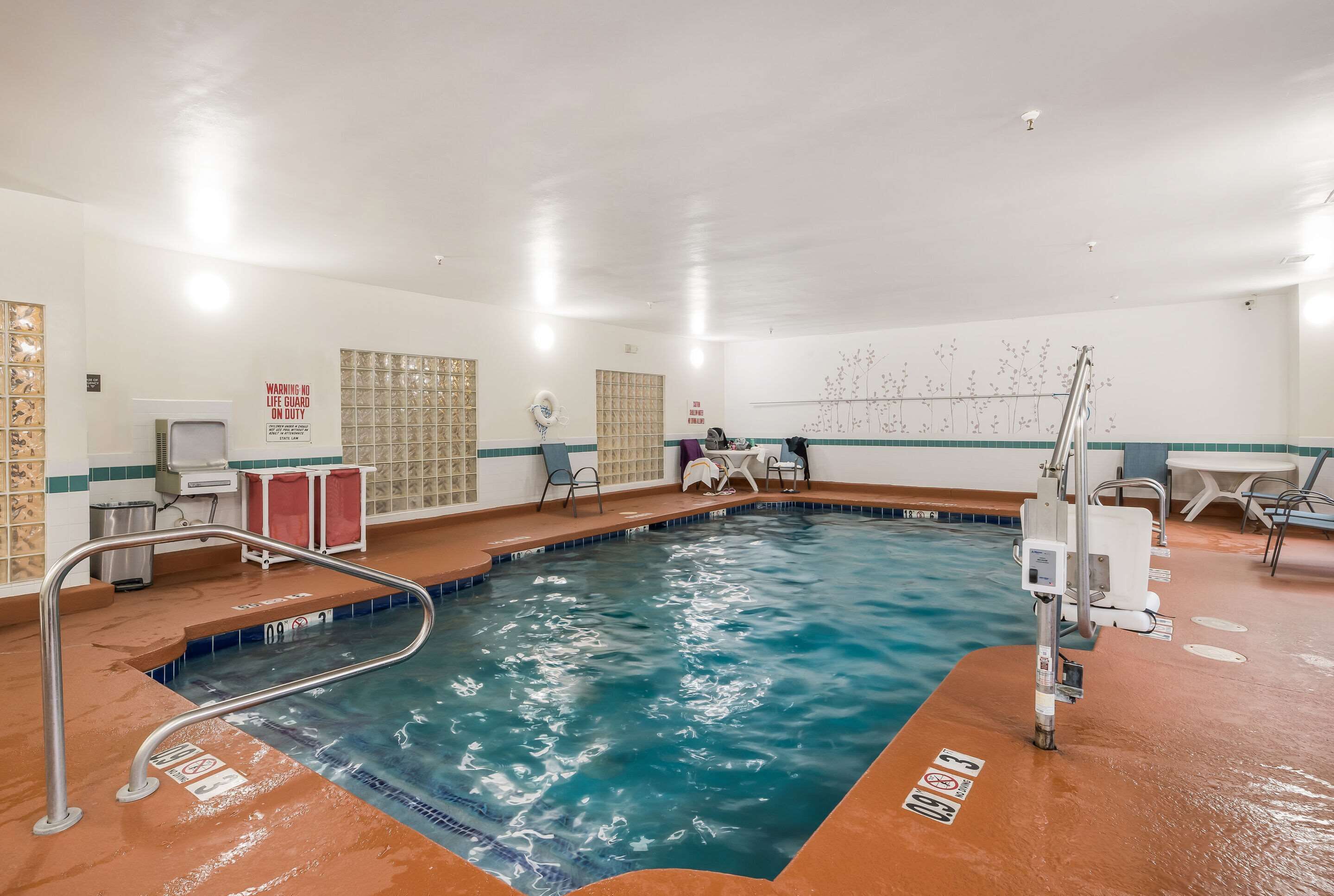An indoor swimming pool with a lifeguard station, poolside chairs, and a clear water depth marking.