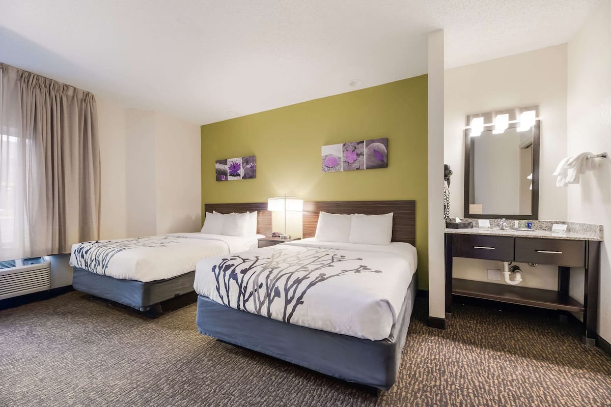 A hotel room with two beds, a bathroom with a vanity, and artwork on the walls.