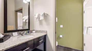 A bathroom with a granite countertop sink, dark cabinets, a large mirror, and a green wall.