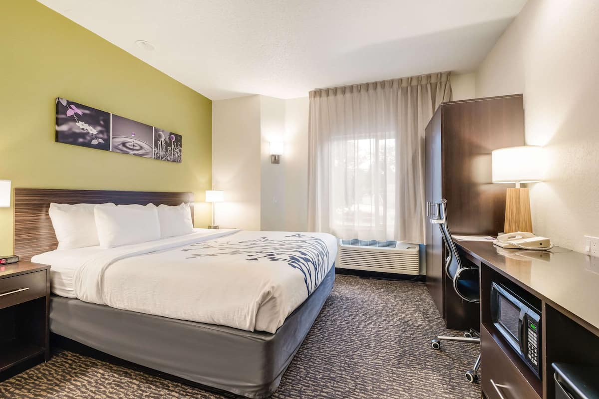 A hotel room with a bed, bedside lamps, a desk with a phone, a microwave, and a window with curtains.