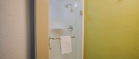 Une douche fermée par des parois de verre, avec une serviette blanche suspendue à une barre métallique.